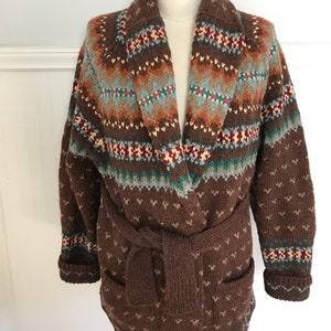Puede incluir: Un c&aacute;rdigan de punto marr&oacute;n con cuello chal y cintur&oacute;n. El c&aacute;rdigan tiene un patr&oacute;n de punto de trenza en marr&oacute;n, crema, azul y verde.