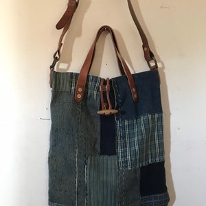 May include: A patchwork tote bag with a brown leather strap and handle. The bag is made of different shades of blue denim and has a unique, rustic look.