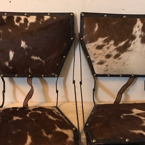 May include: Two chairs with a metal frame and a brown and white cowhide seat and back.