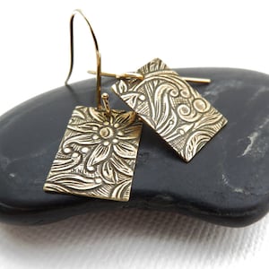 May include: A pair of gold-toned dangle earrings with a floral design. The earrings are rectangular in shape and have a hook closure.