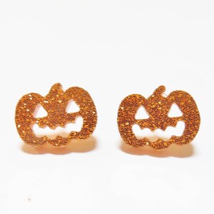 May include: A pair of gold glitter pumpkin earrings. The pumpkins have a jack-o'-lantern face cut out.