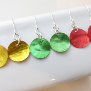 Peut inclure: Six paires de boucles d'oreilles pendantes rondes de couleurs vives. Les boucles d'oreilles sont jaunes, vertes et rouges. Chaque boucle d'oreille a un crochet argenté. Elles sont présentées sur une surface blanche.