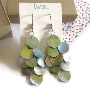 Iridescent natural mussel shell earrings on a display card with the twee logo.  They are resting on a kraft paper cotton filled jewelry box and a colorful piece of decorative paper.