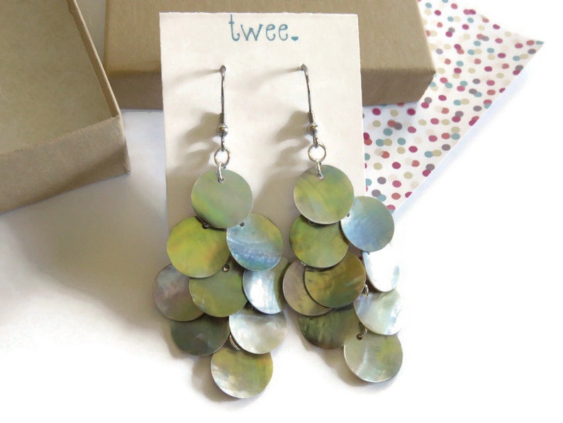 Iridescent natural mussel shell earrings on a display card with the twee logo.  They are resting on a kraft paper cotton filled jewelry box and a colorful piece of decorative paper.