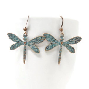 May include: A pair of copper-toned dragonfly earrings with a teal blue patina finish. The earrings have a delicate, detailed design and are perfect for adding a touch of nature to any outfit.