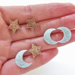 May include: A collection of glittery star and crescent moon-shaped embellishments. The stars are a bronze color, and the moons are silver. These decorative pieces are ideal for craft projects.