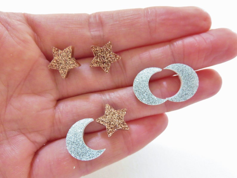 May include: A collection of glittery star and crescent moon-shaped embellishments. The stars are a bronze color, and the moons are silver. These decorative pieces are ideal for craft projects.