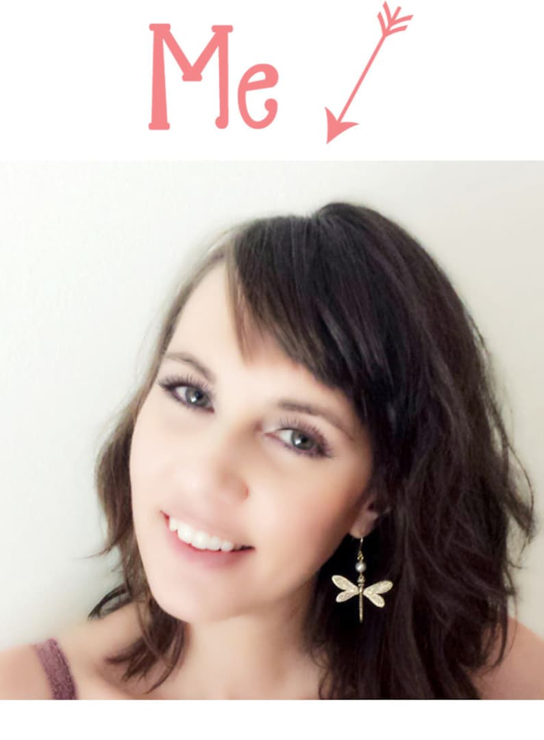 May include: A woman with long brown hair and a smile is wearing a pair of gold dragonfly earrings with a pearl accent.