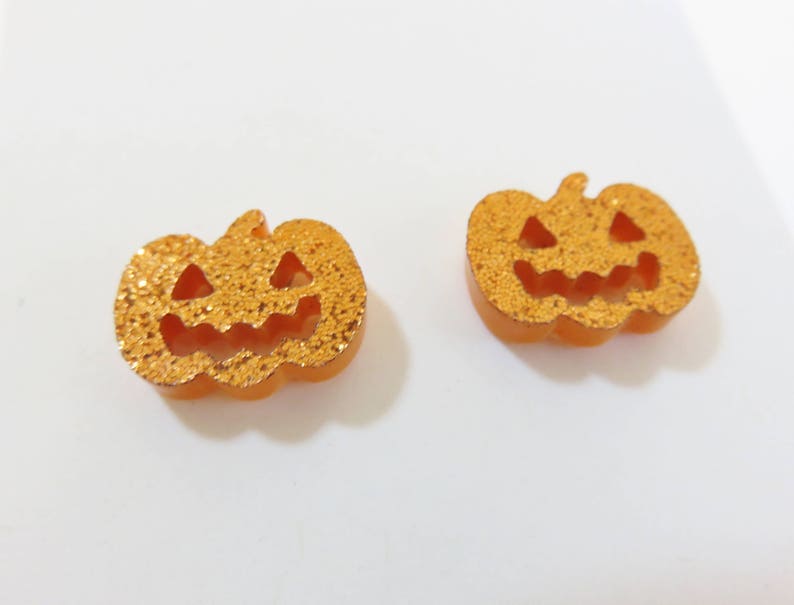 Puede incluir: Dos pendientes de Halloween de color naranja en forma de calabaza con detalles de purpurina y una cara de calabaza.