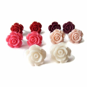 May include: A collection of rose-shaped stud earrings in various colors, including red, pink, peach, and white. The earrings are arranged on a white background, showcasing their detailed floral design. These earrings are a charming accessory.