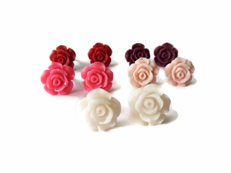 May include: A collection of rose-shaped stud earrings in various colors, including red, pink, peach, and white. The earrings are arranged on a white background, showcasing their detailed floral design. These earrings are a charming accessory.