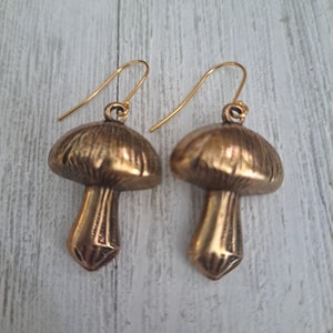 Mushroom earrings in antiqued brass with gold plated ear wires. Shown on a white wood background.