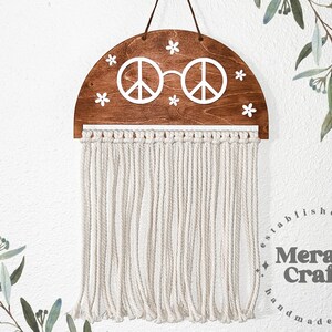 Puede incluir: Una pared de madera en forma de semicírculo con un diseño de signo de paz y gafas. La pared tiene flores blancas y una franja de hilo blanco.