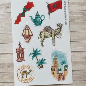 May include: A sticker sheet featuring watercolor illustrations of Moroccan themes, including a map of Morocco, a red flag with a green star, a teal teapot, a camel, two lanterns, palm trees, a circular Morocco emblem, and a mosque with the text WWW.MARYLINEWEYL.COM.