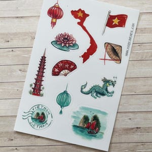 Op de afbeelding: Een stickervel met diverse illustraties gerelateerd aan Vietnam, waaronder een rode kaart met een gele ster, een rode lantaarn, een lotusbloem, een conische hoed, een pagode, een rode waaier, een groene draak en een bootscène.