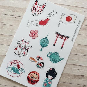 May include: A sticker sheet featuring various illustrations including a fox mask, a map of Japan, a Japanese flag, a cherry blossom, a lantern, a torii gate, a beckoning cat, sushi, a teapot, a mountain emblem with the text JAPON, a Daruma doll, and a kokeshi doll.