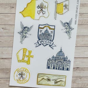 May include: A sticker sheet featuring watercolour illustrations of Vatican-themed icons, including the flag, St. Peter's Basilica, cherubs, a mitre, a cross, and the Creation of Adam. The text "VATICAN" appears on a shield and a circular emblem.