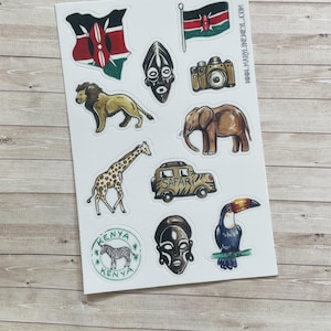 Può includere: Un foglio di adesivi con illustrazioni della bandiera del Kenya, una mappa del Kenya, un leone, un elefante, una giraffa, una zebra, un tucano, due maschere tribali, una fotocamera e un veicolo da safari. Il testo WWW.MARYLINEWEYL.COM è stampato sul foglio.