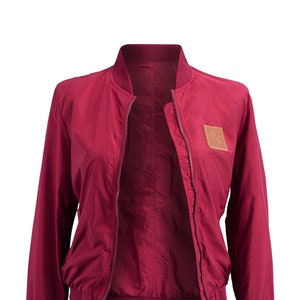 May include: A burgundy bomber jacket with a zipper closure and a brown leather patch on the left side.