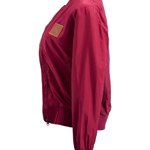 May include: A burgundy bomber jacket with a zipper closure and a brown leather patch on the left chest.