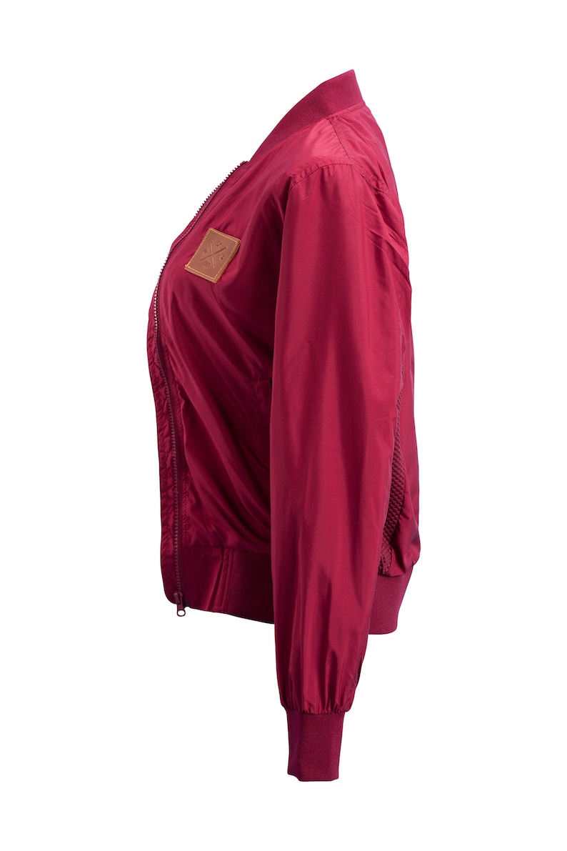 May include: A burgundy bomber jacket with a zipper closure and a brown leather patch on the left chest.
