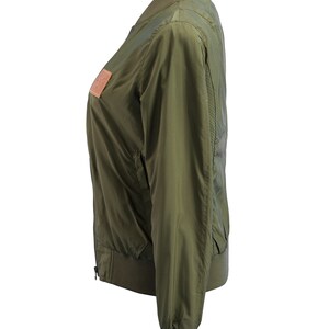 May include: A green bomber jacket with a zipper closure and a brown leather patch on the left side.