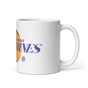 Könnte beinhalten: Weiße Keramiktasse mit einem Basketball-Motiv in Lila und Orange und dem Text "Black-Hole Mines" mit einem eingetragenen Warenzeichen.