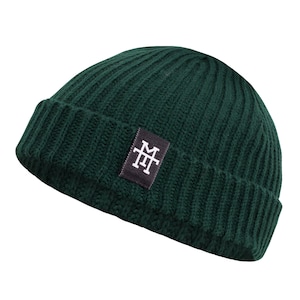 Könnte beinhalten: Eine dunkelgrüne Strickmütze mit einem schwarzen Patch, auf dem die weißen Buchstaben "MT" in einem Monogramm-Stil stehen.