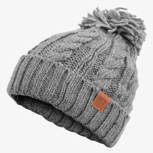 Könnte beinhalten: Graue Strickmütze mit Bommel oben und einem braunen Lederpatch mit dem Text "113" an der Seite.