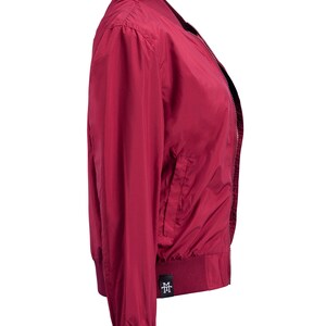May include: A burgundy bomber jacket with a zipper closure and a small logo on the left side. The jacket has a ribbed collar, cuffs, and hem.