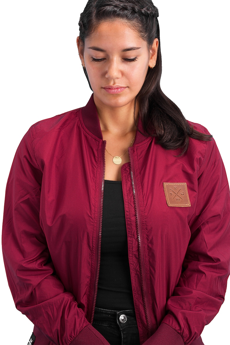 May include: A maroon bomber jacket with a brown leather patch on the left side featuring a cross and the text "1973".