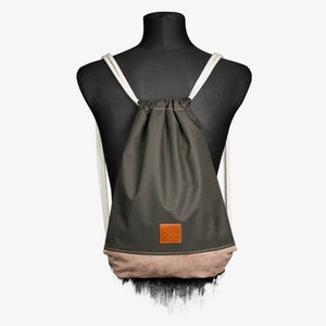 Könnte beinhalten: Ein dunkelgrüner Rucksack mit Kordelzug und einem braunen Lederflicken. Der Rucksack hat weiße Kordeln und einen beigefarbenen Boden.