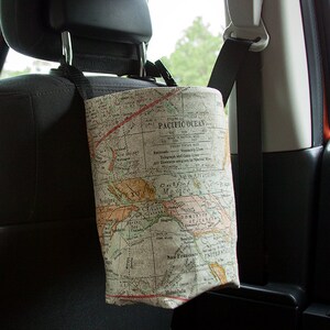 May include: A car seat back organizer with a map print design. The organizer is made of fabric and has a drawstring closure. It is hanging from the headrest of a car seat.