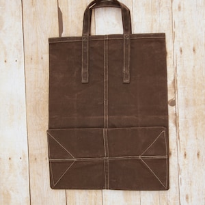 Pu&ograve; includere: Una borsa tote in tela marrone con una grande tasca sul davanti. La borsa ha due manici ed &egrave; realizzata in un materiale resistente.