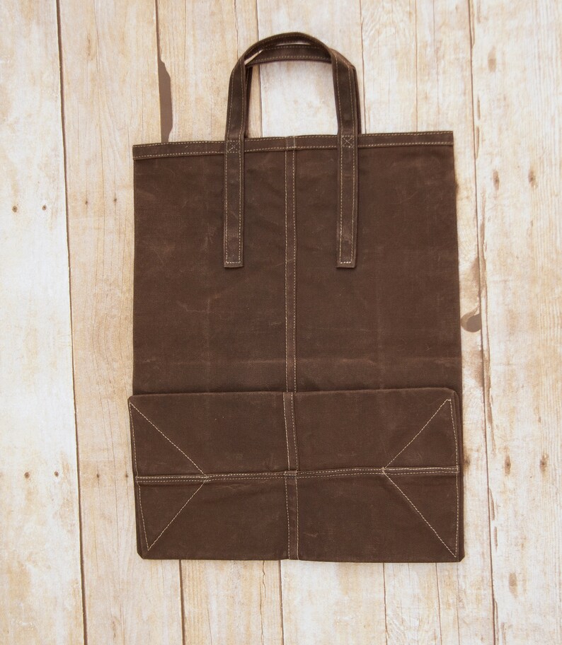 Pu&ograve; includere: Una borsa tote in tela marrone con una grande tasca sul davanti. La borsa ha due manici ed &egrave; realizzata in un materiale resistente.