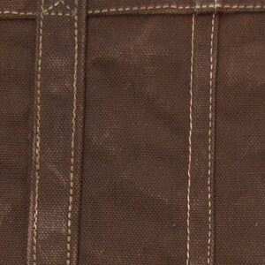 Pu&ograve; includere: Primo piano di una borsa tote in tela marrone con una tracolla in pelle marrone e cuciture bianche. La borsa ha un design semplice ed &egrave; realizzata in materiale resistente.