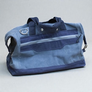 May include: A blue and navy duffel bag with a zipper closure and two handles. The bag has a shoulder strap and a silver metal ring on the side. The bag is made of a durable material and is suitable for travel or everyday use.