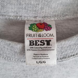 May include: A light gray sweatshirt featuring a white interior garment tag with the Fruit of the Loom logo, the word BEST, and fabric composition of 50% cotton and 50% polyester. The tag indicates the item is size L and made in Honduras.