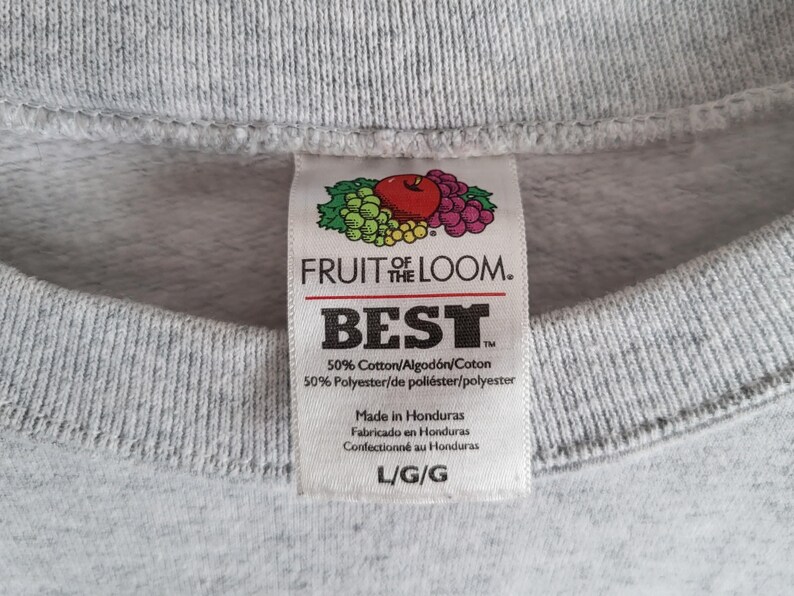 May include: A light gray sweatshirt featuring a white interior garment tag with the Fruit of the Loom logo, the word BEST, and fabric composition of 50% cotton and 50% polyester. The tag indicates the item is size L and made in Honduras.