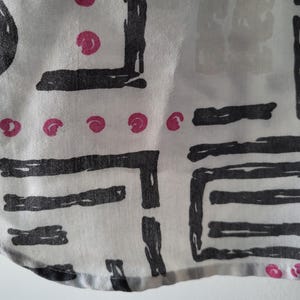 Puede incluir: Primer plano de una tela blanca con un patr&oacute;n repetitivo de formas geom&eacute;tricas negras y peque&ntilde;os c&iacute;rculos rosas. La tela tiene un aspecto ligeramente texturizado y un borde curvo.