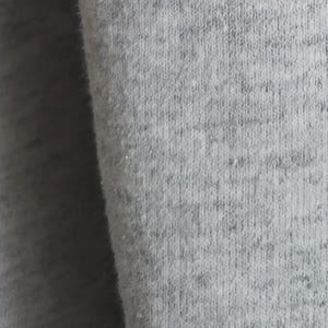 May include: A close-up view of light gray heathered fabric featuring a soft, fleecy texture. The material displays a subtle speckled pattern with varying shades of gray, creating a consistent, woven appearance across the entire surface of the textile.