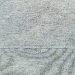 May include: A light gray heathered fabric with a textured knit surface. The material features a horizontal ribbed hemline at the bottom edge, with visible light yellow discoloration spots scattered across the fabric surface.