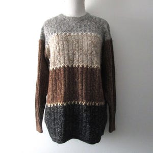 May include: A striped sweater with a grey, beige, brown, and black color scheme. The sweater has a crew neck and long sleeves.