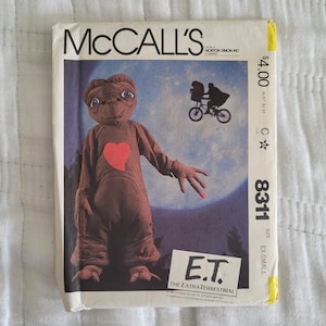 May include: McCall's sewing pattern featuring E.T. The Extra-Terrestrial. The cover art shows E.T. with a red heart, a silhouette of a bicycle with two riders, and the movie title. The pattern is size EX-SMALL.