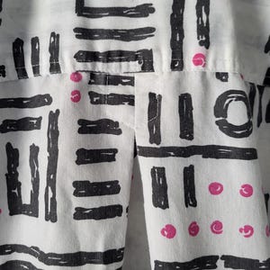 Puede incluir: Primer plano de una tela blanca con un patr&oacute;n geom&eacute;trico negro repetido de l&iacute;neas y rect&aacute;ngulos. Peque&ntilde;os c&iacute;rculos rosas est&aacute;n dispersos en el dise&ntilde;o. La tela parece ser parte de una prenda.