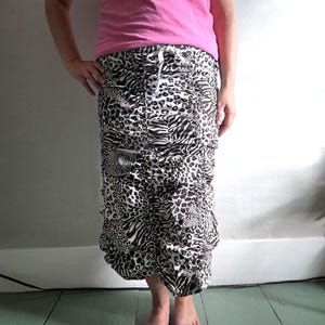 May include: A midi-length skirt featuring a black and white animal print pattern with a mix of leopard and zebra designs. The skirt has a gathered, ruched texture running vertically down the front and includes a white drawstring at the waist.