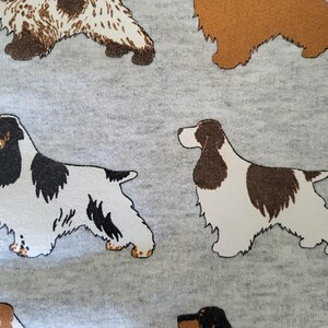 May include: A light gray fabric featuring a repeating pattern of spaniel dogs in various color combinations, including solid brown, white with black patches, and white with brown patches, all depicted in a side profile standing position.