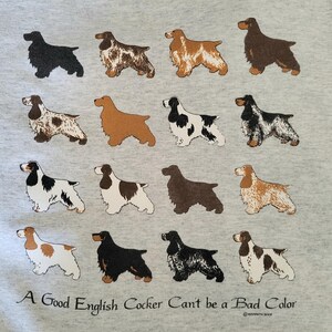 May include: A light gray sweatshirt featuring a grid of sixteen illustrations of English Cocker Spaniels in various coat colors and patterns. Below the dogs, the text reads: A Good English Cocker Can't be a Bad Color in black lettering.