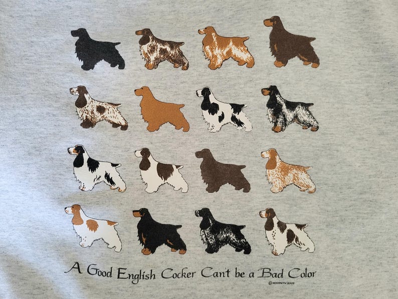 May include: A light gray sweatshirt featuring a grid of sixteen illustrations of English Cocker Spaniels in various coat colors and patterns. Below the dogs, the text reads: A Good English Cocker Can't be a Bad Color in black lettering.