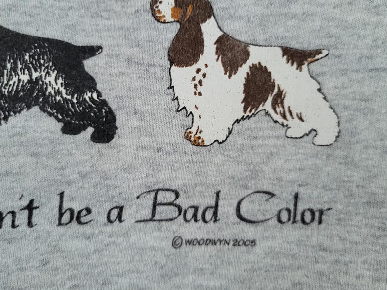 May include: A heather gray fabric featuring a black dog and a brown and white dog illustration. Below the dogs, the text reads "n't be a Bad Color" with the copyright text "&copy; WOODWYN 2005" printed underneath in black ink.